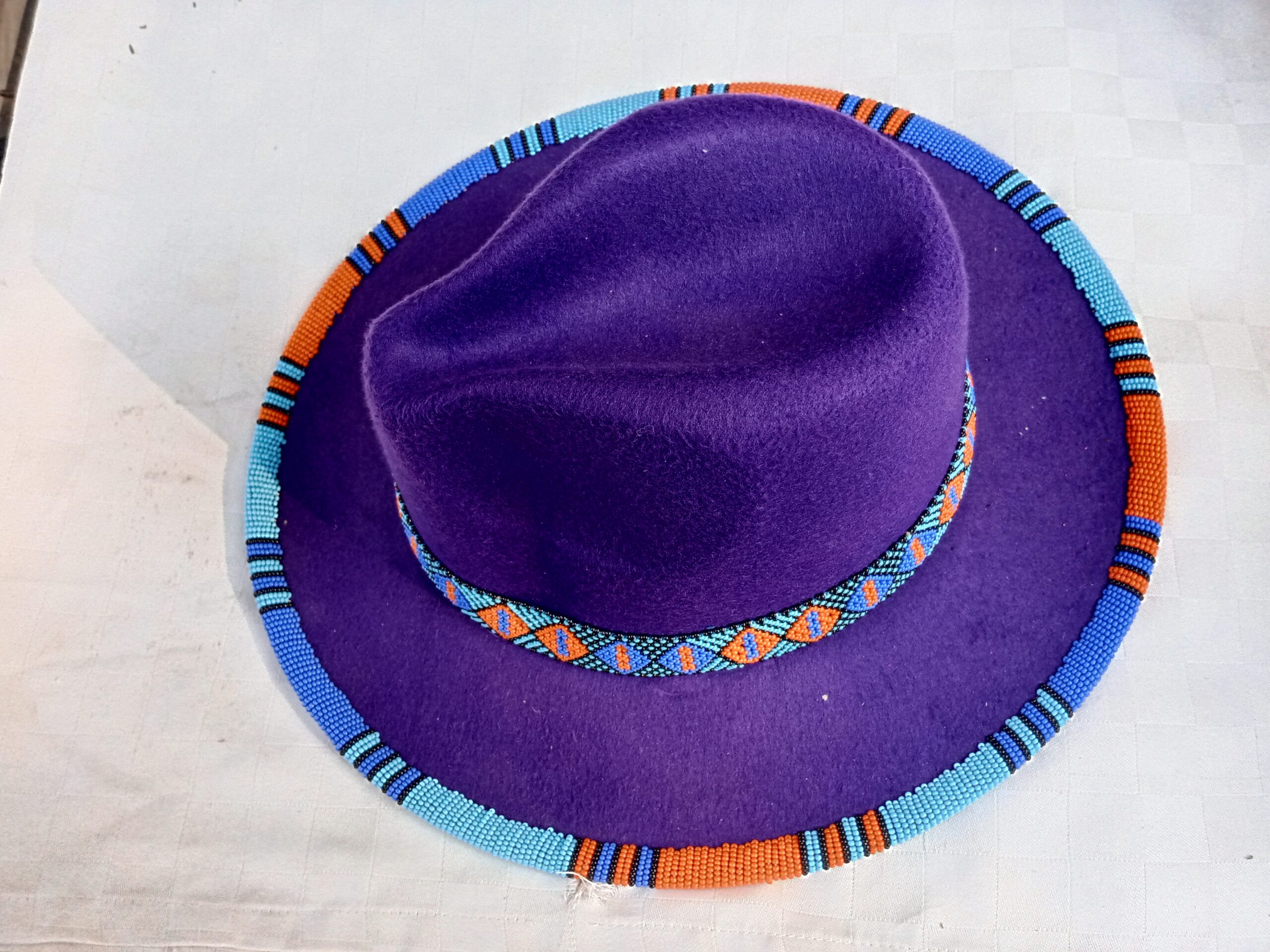 Wide-brim felt fedora with a hand-beaded zigzag trim along the brim and crown — a bold, handmade statement hat available in multiple colors.