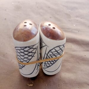 Store A collection of handcrafted salt shaker pairs made from bone with a smooth ivory-white base, each topped with a polished wooden dome for a warm two-tone contrast. The etched detailing varies across pieces — from crosshatch and swirl motifs to bold spotted and wavy zigzag patterns — giving each pair its own distinct character while sharing the same handmade quality. Small holes drilled into the wooden tops allow for easy, controlled shaking. Sold as matching pairs, these shakers bring a rustic, artisan touch to any table setting.